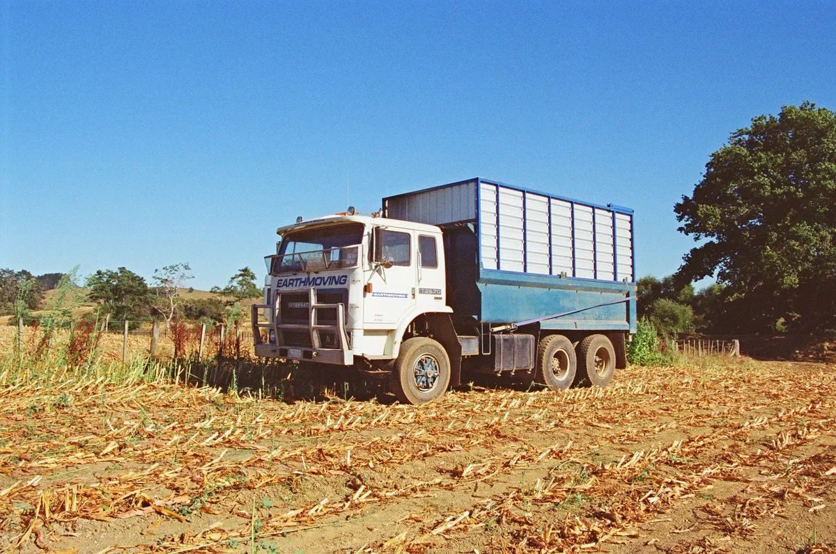 White truck with a tall blue and white silage bin, parked in a harvested maize paddock under a clear blue sky