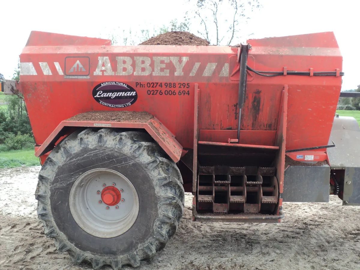 Side of an orange Abbey muck spreader carrying the Langman Agricultural Contracting oval and two phone numbers, loaded with compost