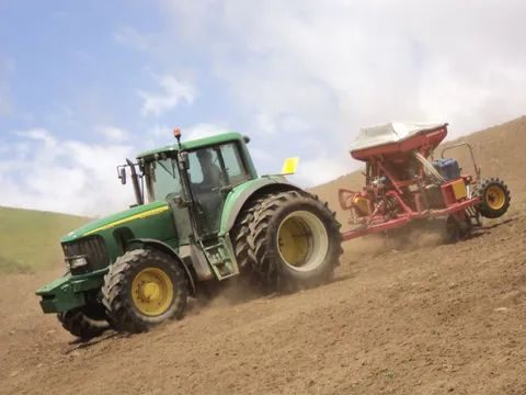 John Deere tractor towing a red air seeder up a freshly worked slope